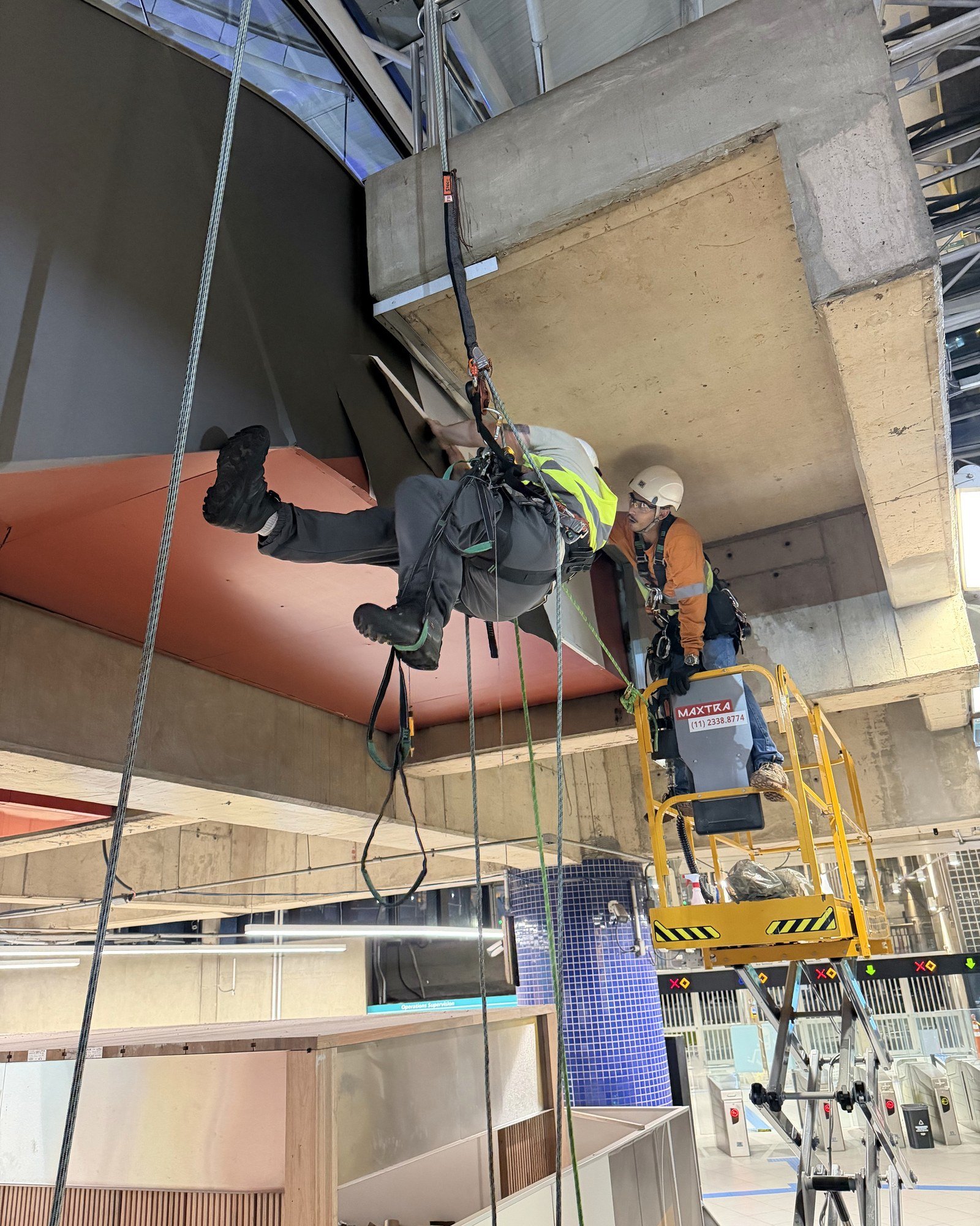 Dois técnicos da Eleva em corda instalando um painel curvo no teto de um terminal